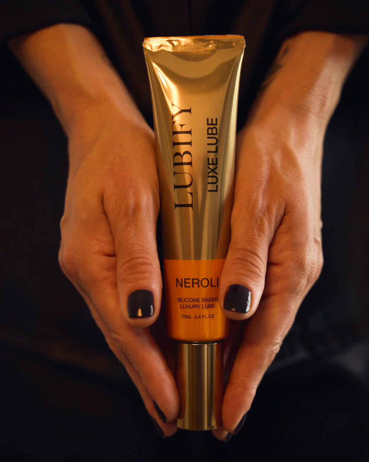 Hands holding a gold tube labeled 'Lubify Luxe Lube Neroli.'