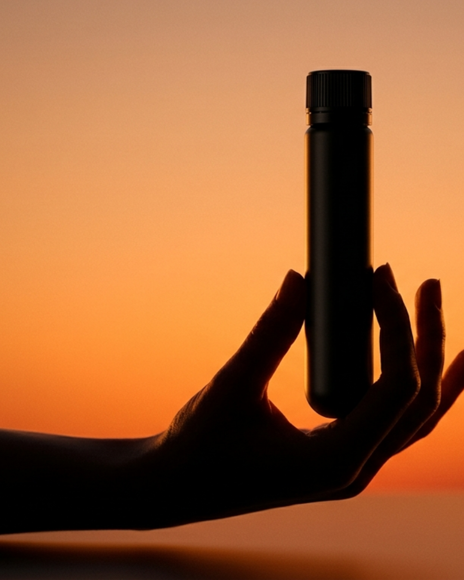 A silhouetted hand holding a small black bottle against an orange sky at sunset.