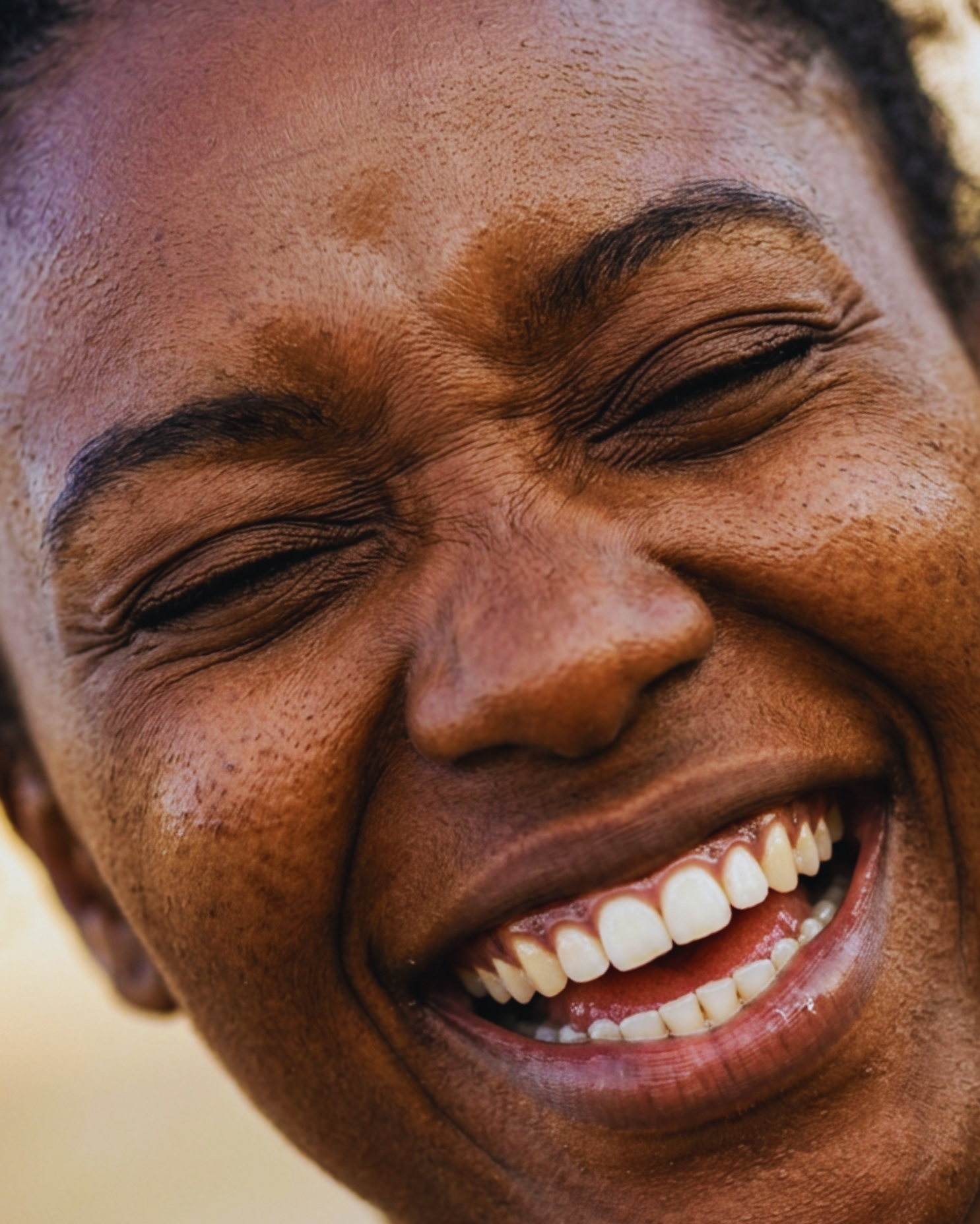 A close-up photograph of a Black person laughing with their eyes crinkled shut.