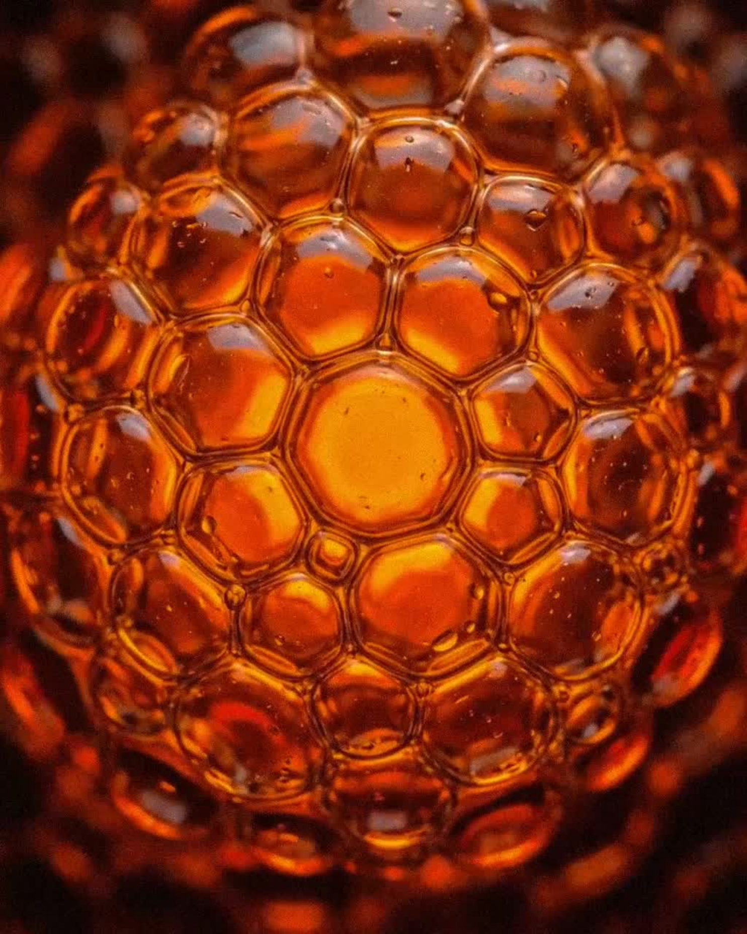 An extreme close-up of a spherical cluster of glowing, amber-colored bubbles.