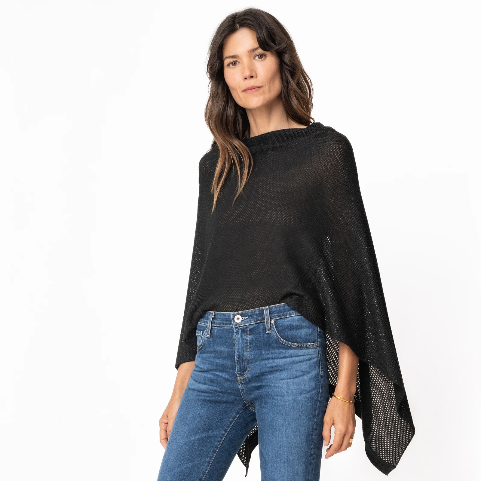 Person wearing a black poncho and blue jeans against a white background.