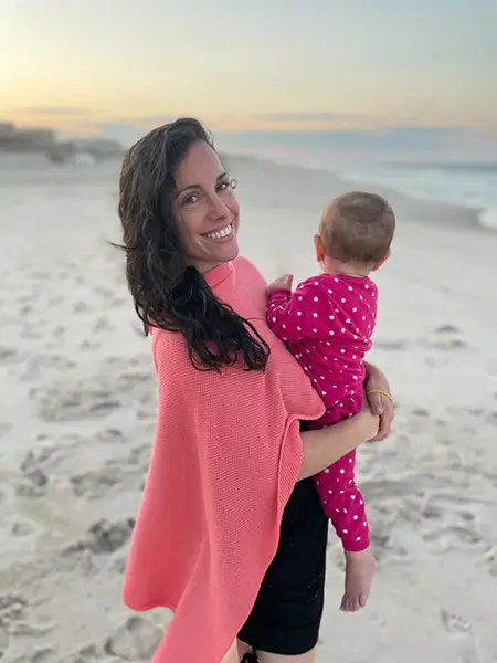 Woman holding a baby on a beach at sunset.