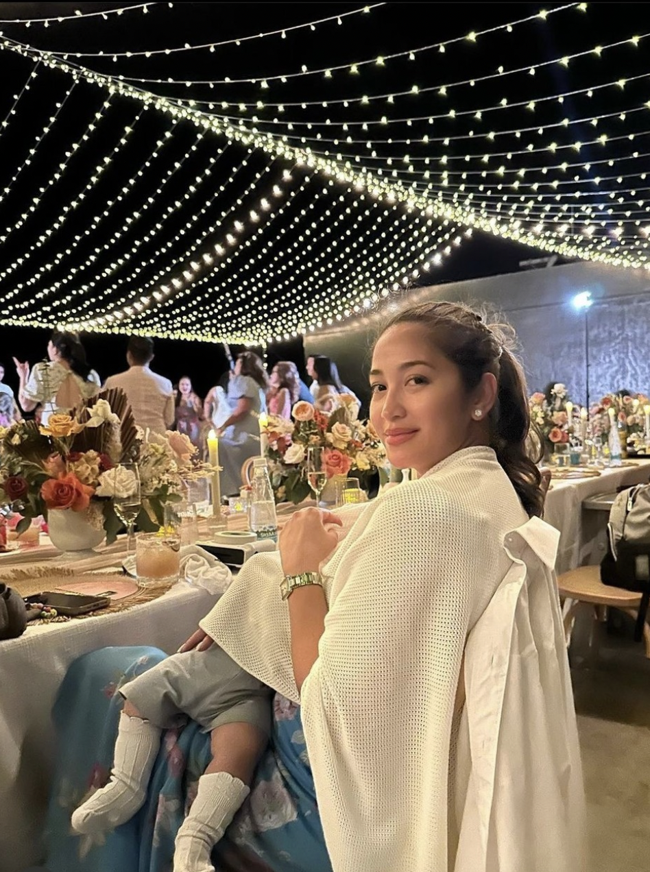Woman holding a baby at a decorated outdoor event with string lights.
