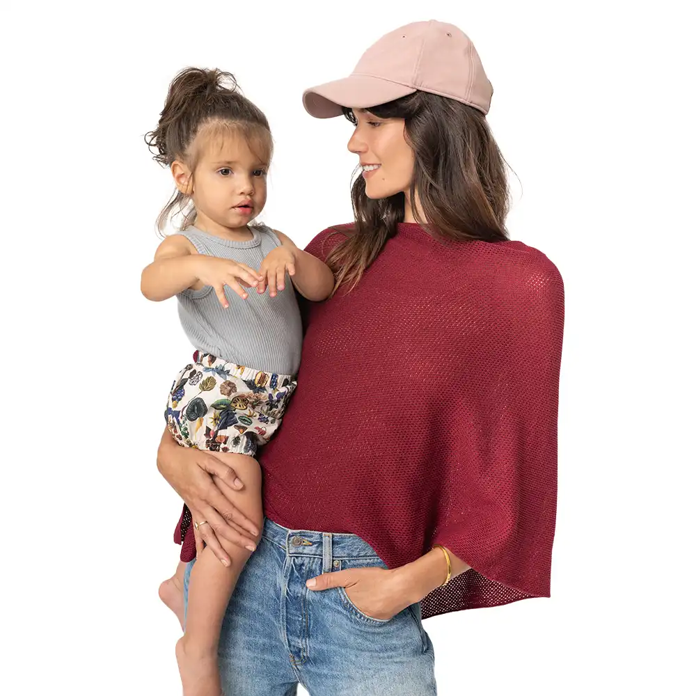Woman in red top holding a child wearing a gray tank top and patterned shorts.
