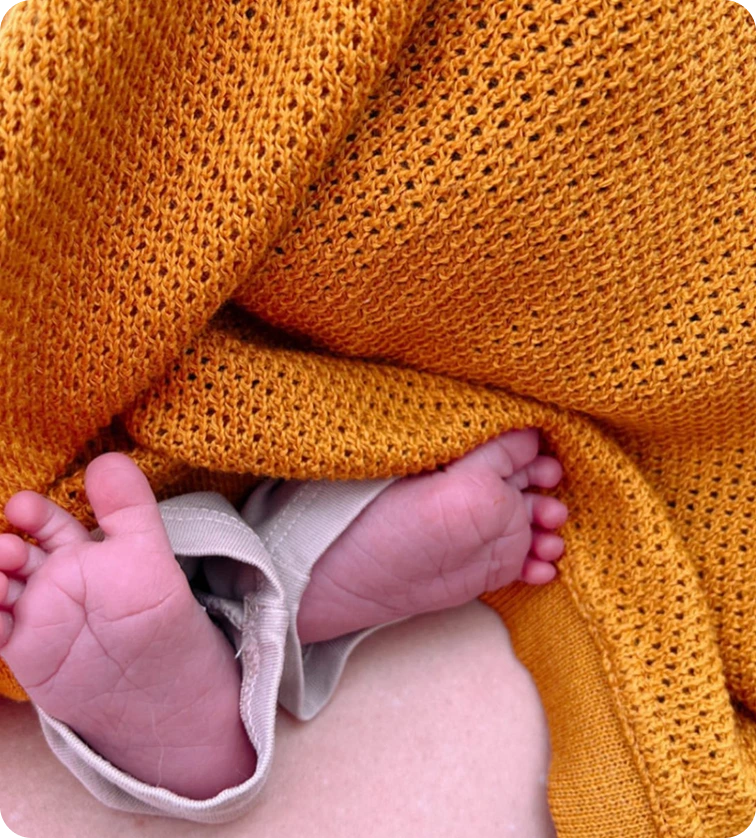 Baby feet wrapped in a yellow knitted blanket.