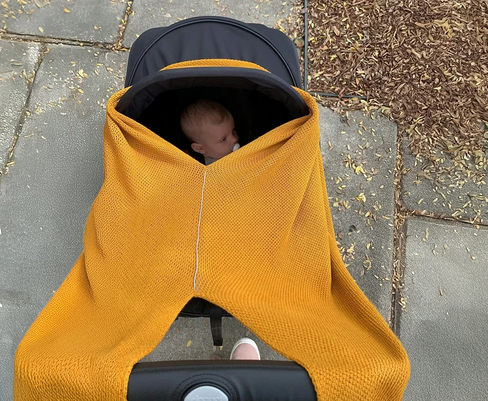 A top-down view of a baby with a pacifier in a stroller, covered by a large yellow blanket.