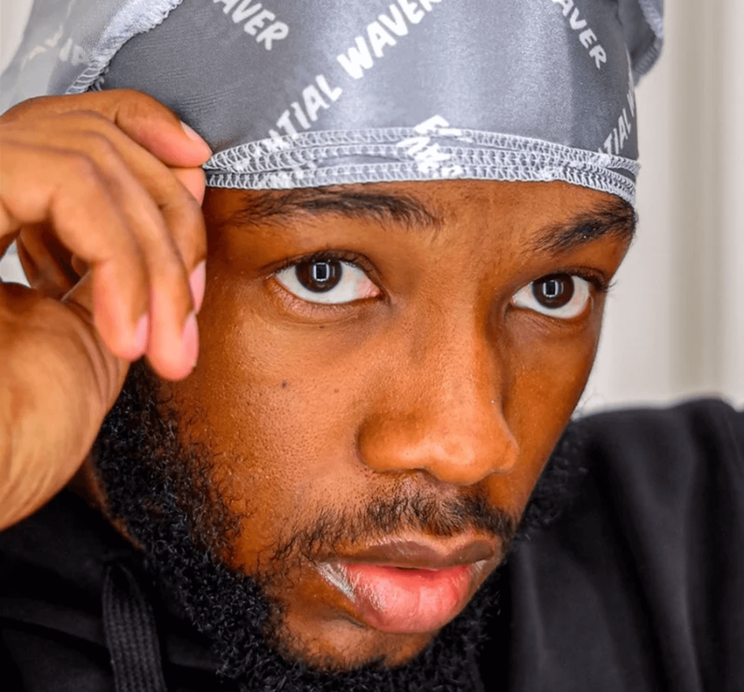 Close-up of a man wearing a silver durag, touching the edge.