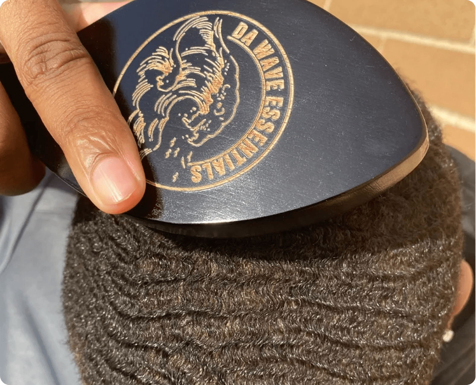 A hand brushing short, wavy hair with a da wave essentials brush.