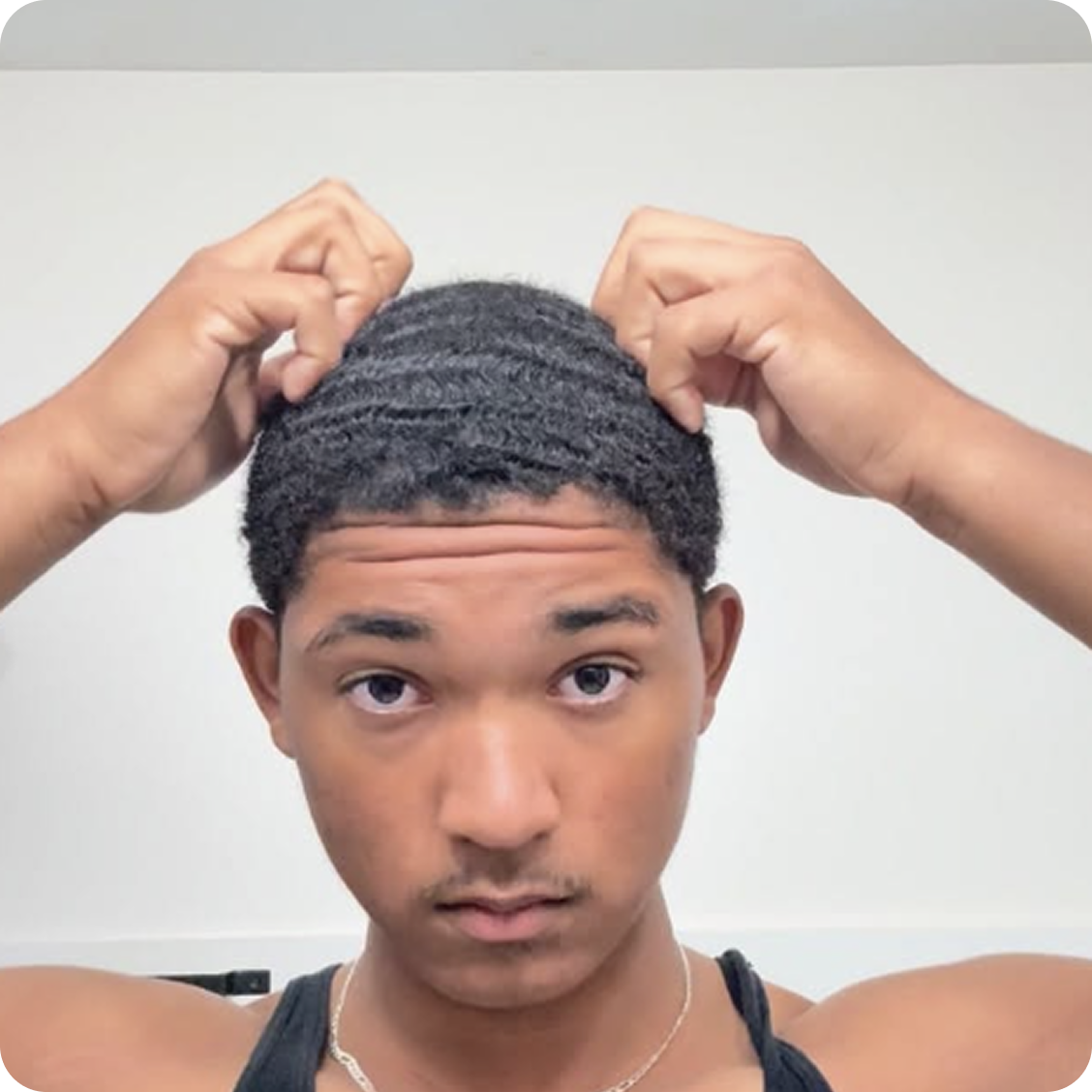 A young man with a waves hairstyle looks at the camera while touching his hair.