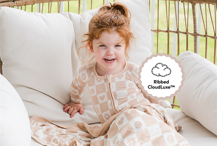 A smiling young girl with red hair sits in a wicker chair wearing tan and white patterned pajamas.