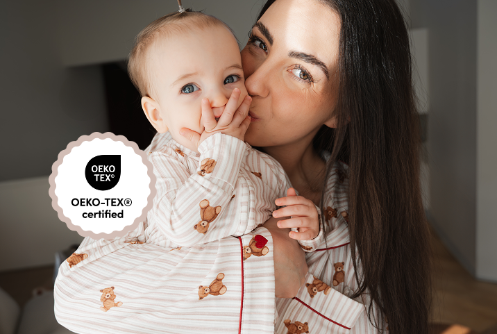 A woman holds a baby and kisses its cheek while they both wear matching teddy bear pajamas.