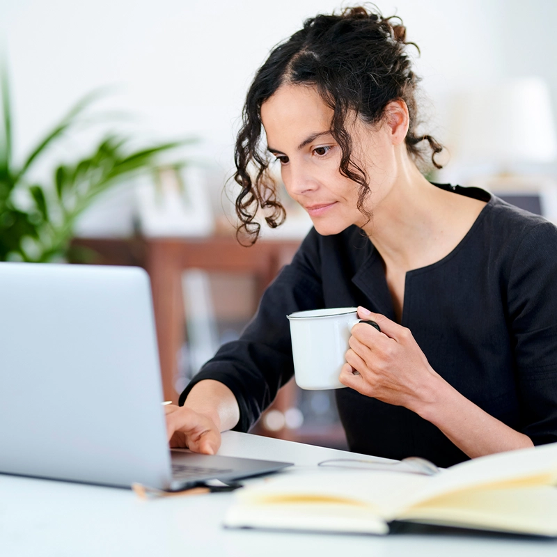 Person holding a mug, working on a laptop at a desk.