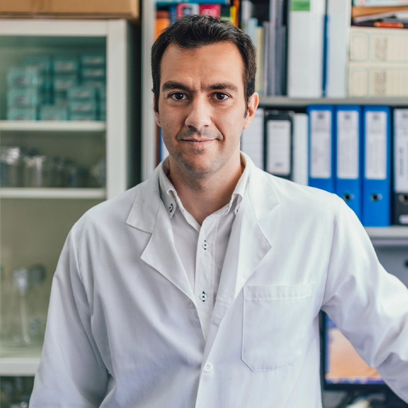Person in a white lab coat standing in front of shelves with binders and boxes.