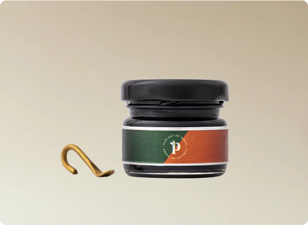 Small jar with a black lid and a green-orange label, next to a gold hook.