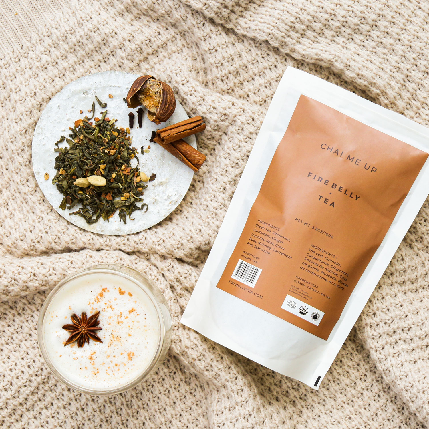 A glass of chai tea with spices and a Firebelly Tea package on a cozy blanket.