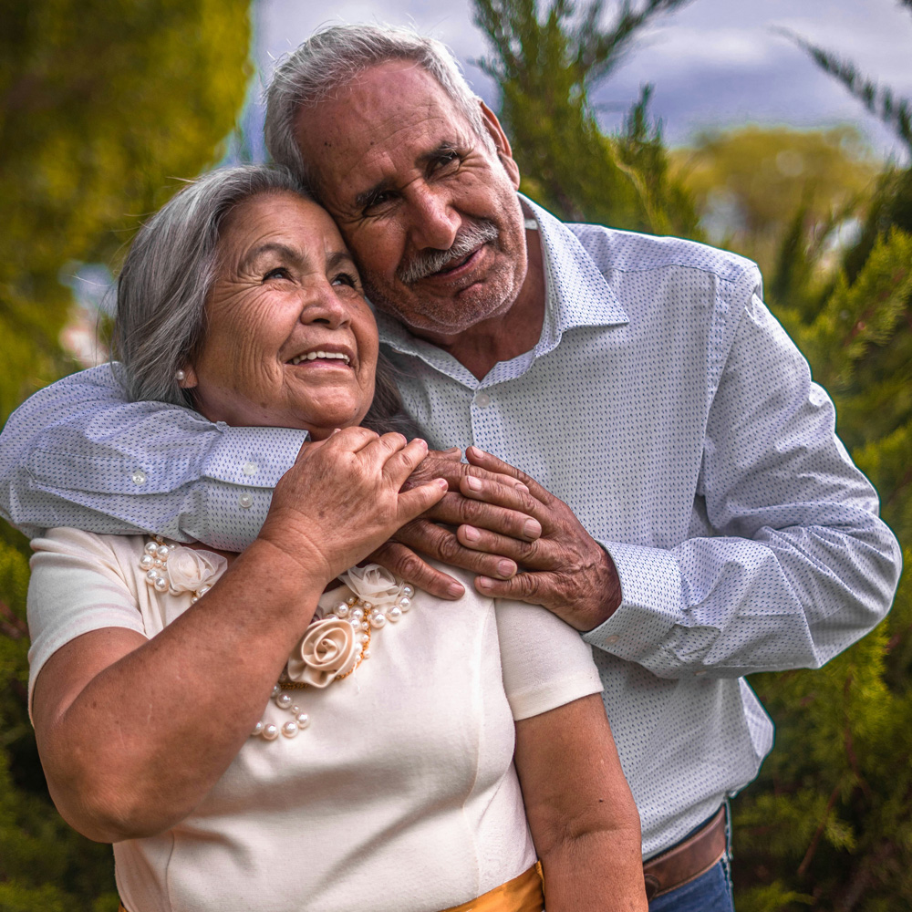 Elderly couple embracing and smiling in a garden setting.