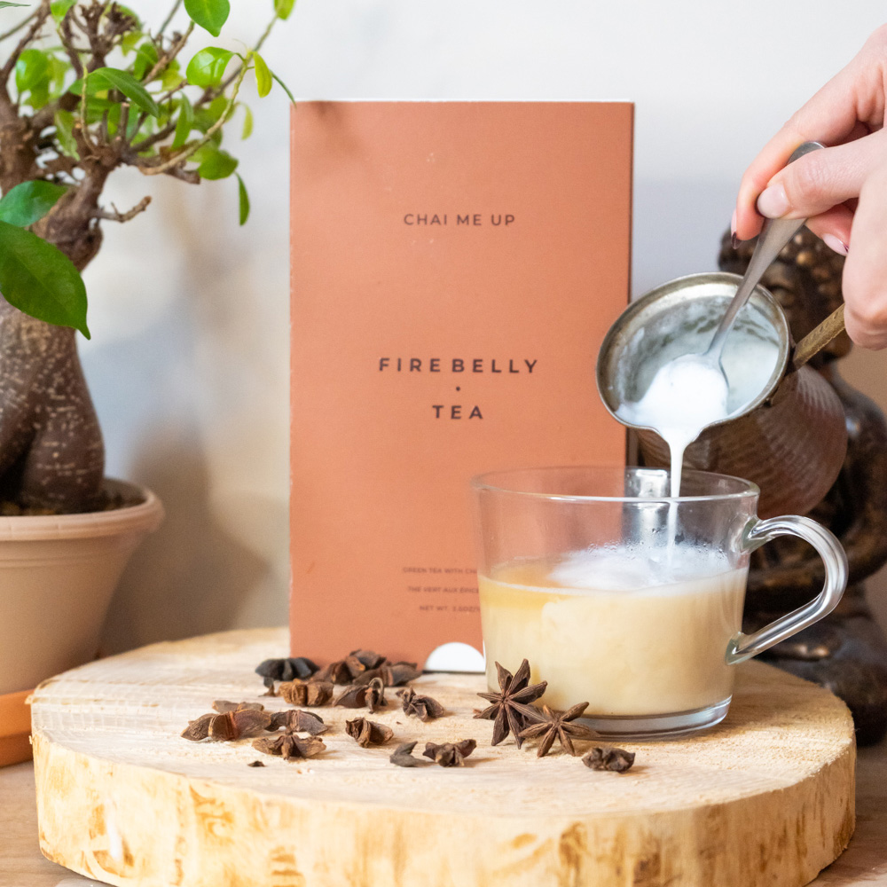 Pouring milk into a glass of chai tea with a Firebelly Tea package nearby.