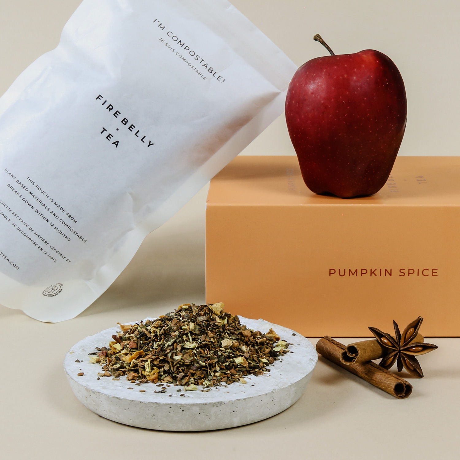 Compostable tea packaging with loose tea, apple, cinnamon, and star anise on a beige background.