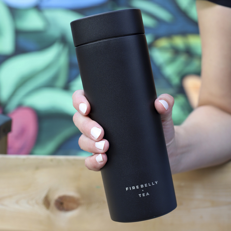 A hand holding a black Firebelly Tea tumbler.