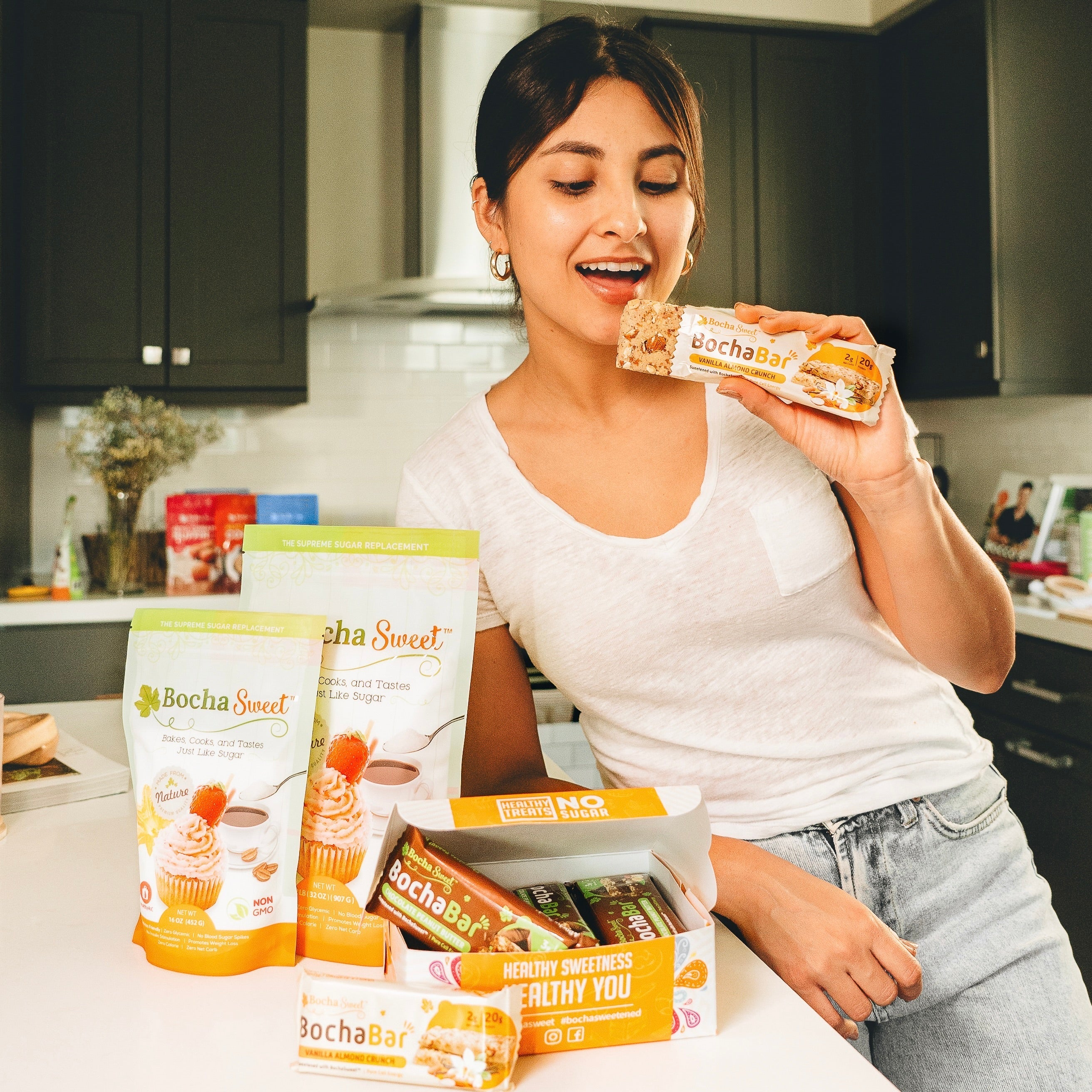 Person in kitchen holding a BochaBar, surrounded by Bocha Sweet products.