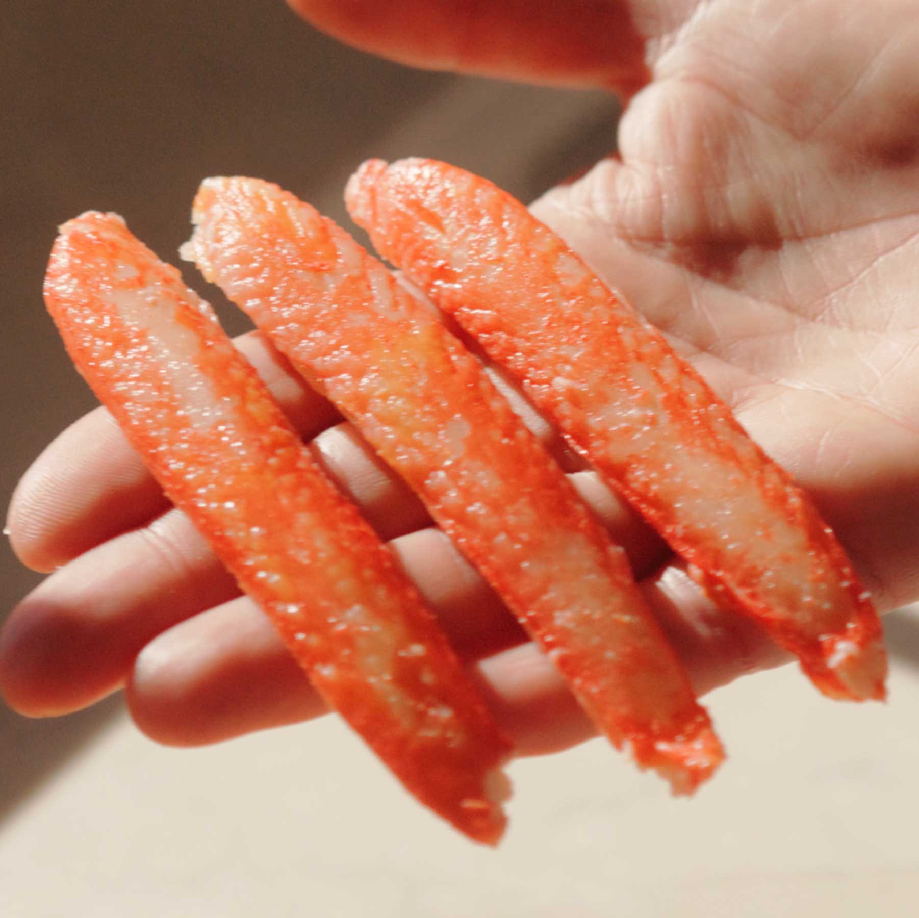 A close-up shot of a hand holding three pieces of cooked crab meat.