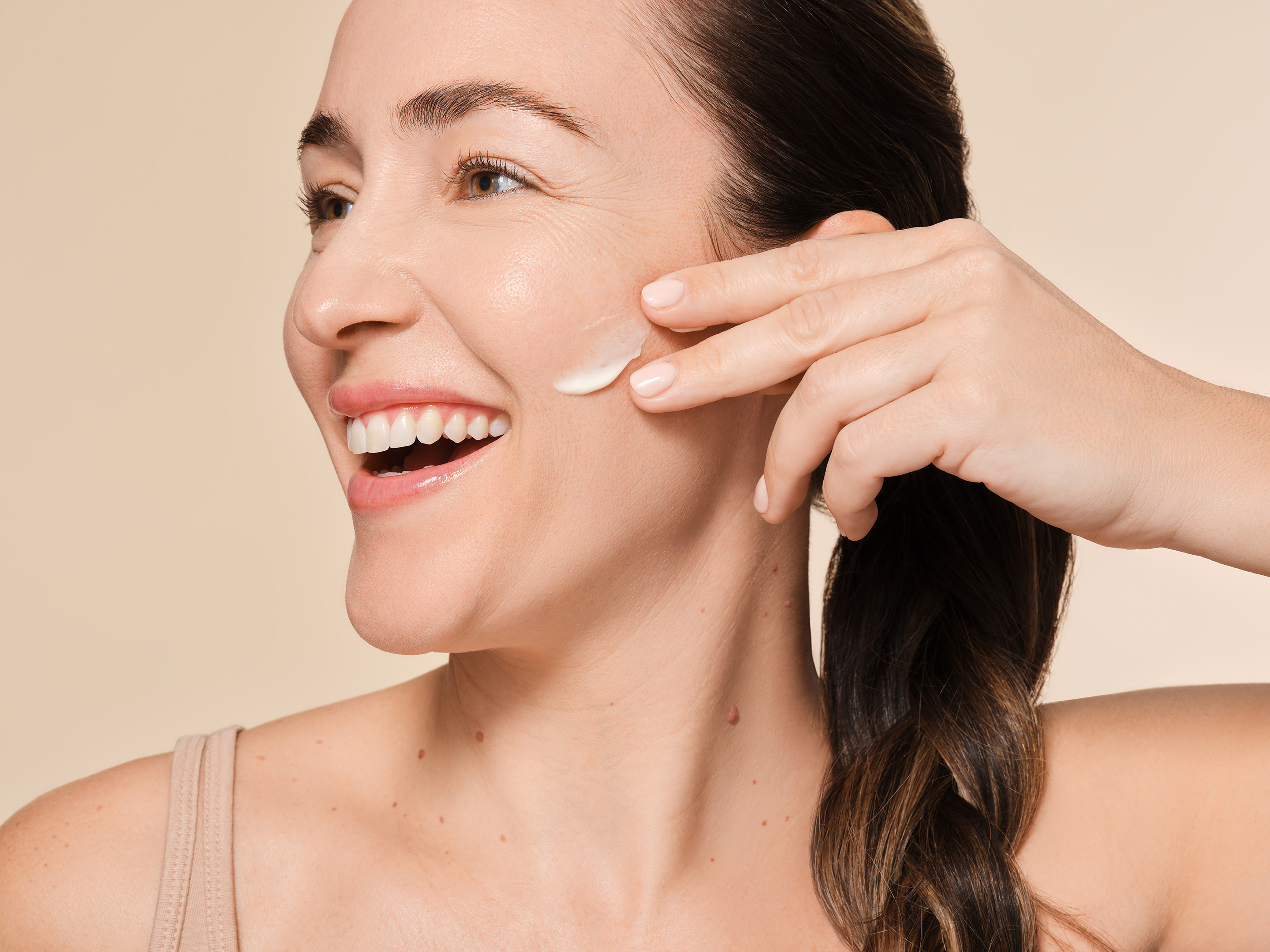 Smiling person applying cream to their cheek.