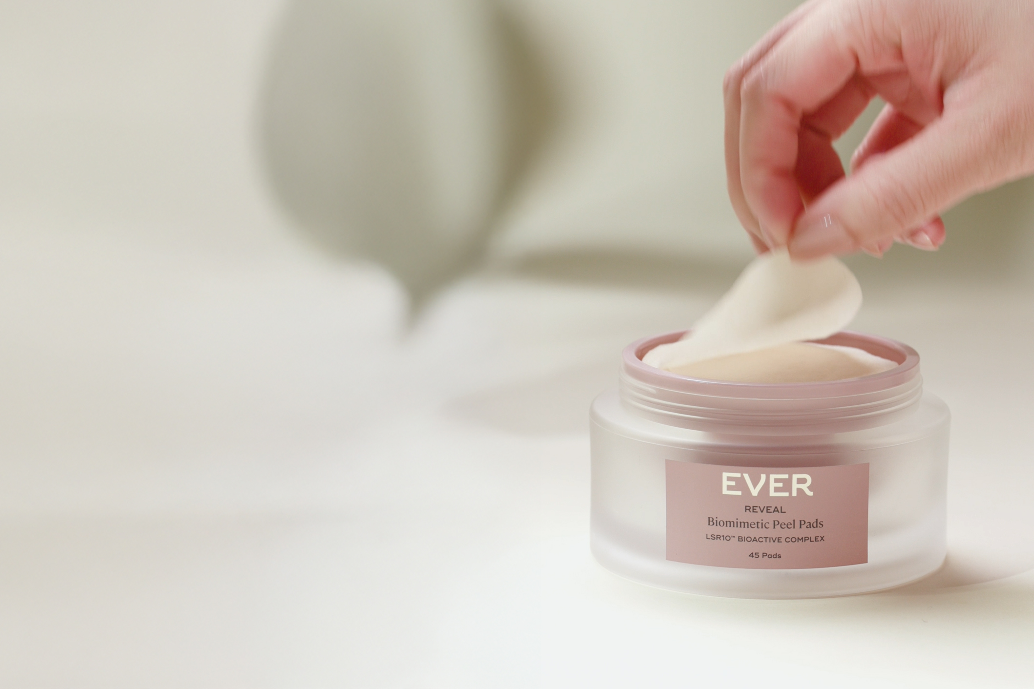 Hand removing pad from a jar labeled 'Ever Reveal Biomimetic Peel Pads'.