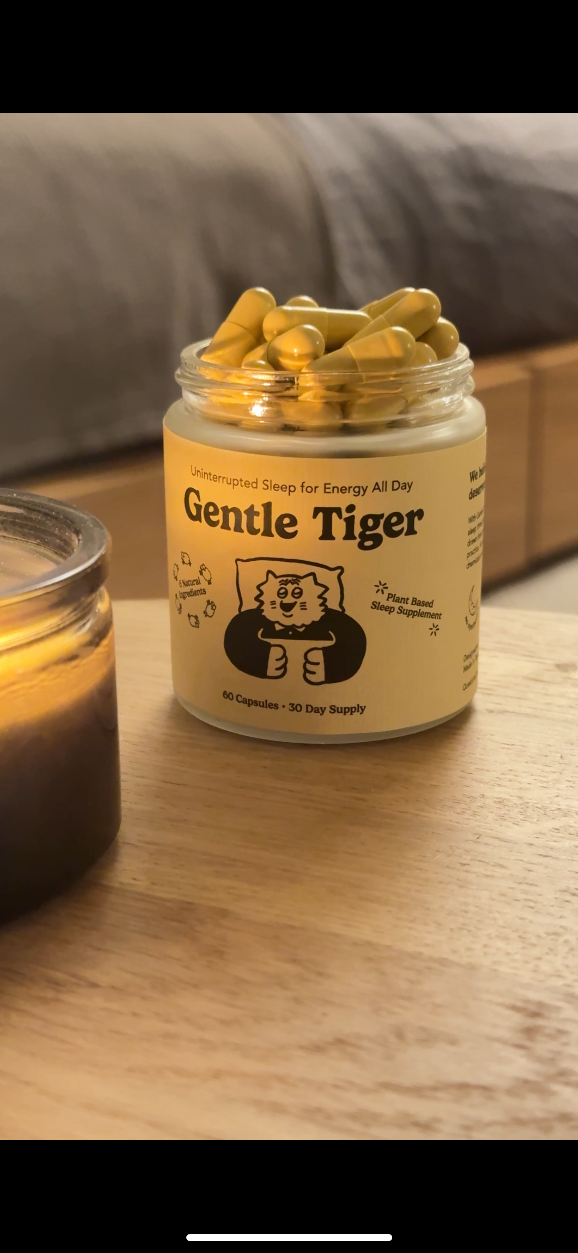 Jar of capsules labeled 'Gentle Tiger' on a wooden surface beside a candle.