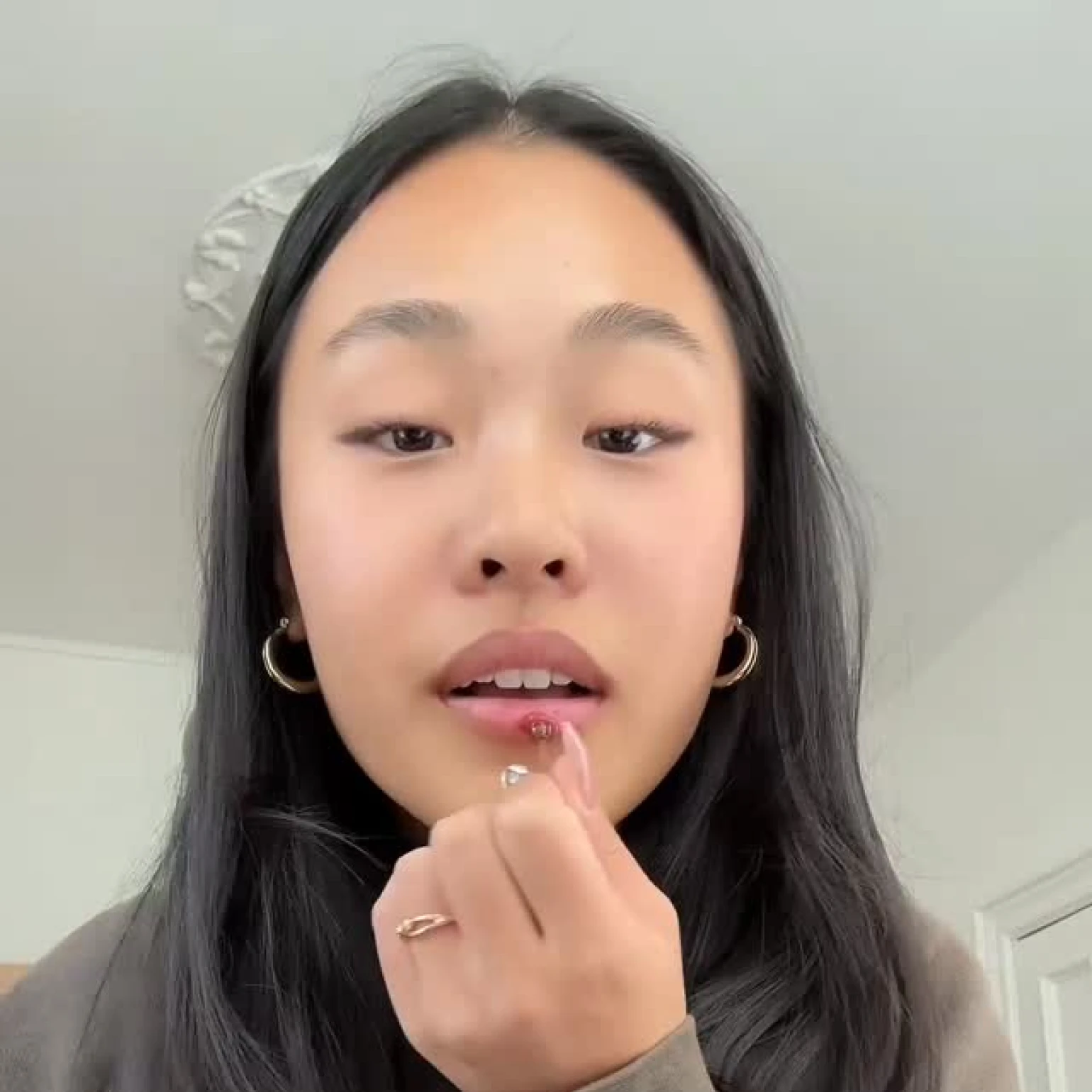 Person applying lip gloss with finger indoors.
