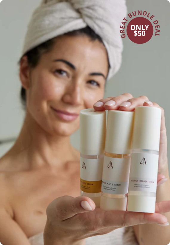 A smiling woman with a towel on her head holds three bottles of skincare serum.