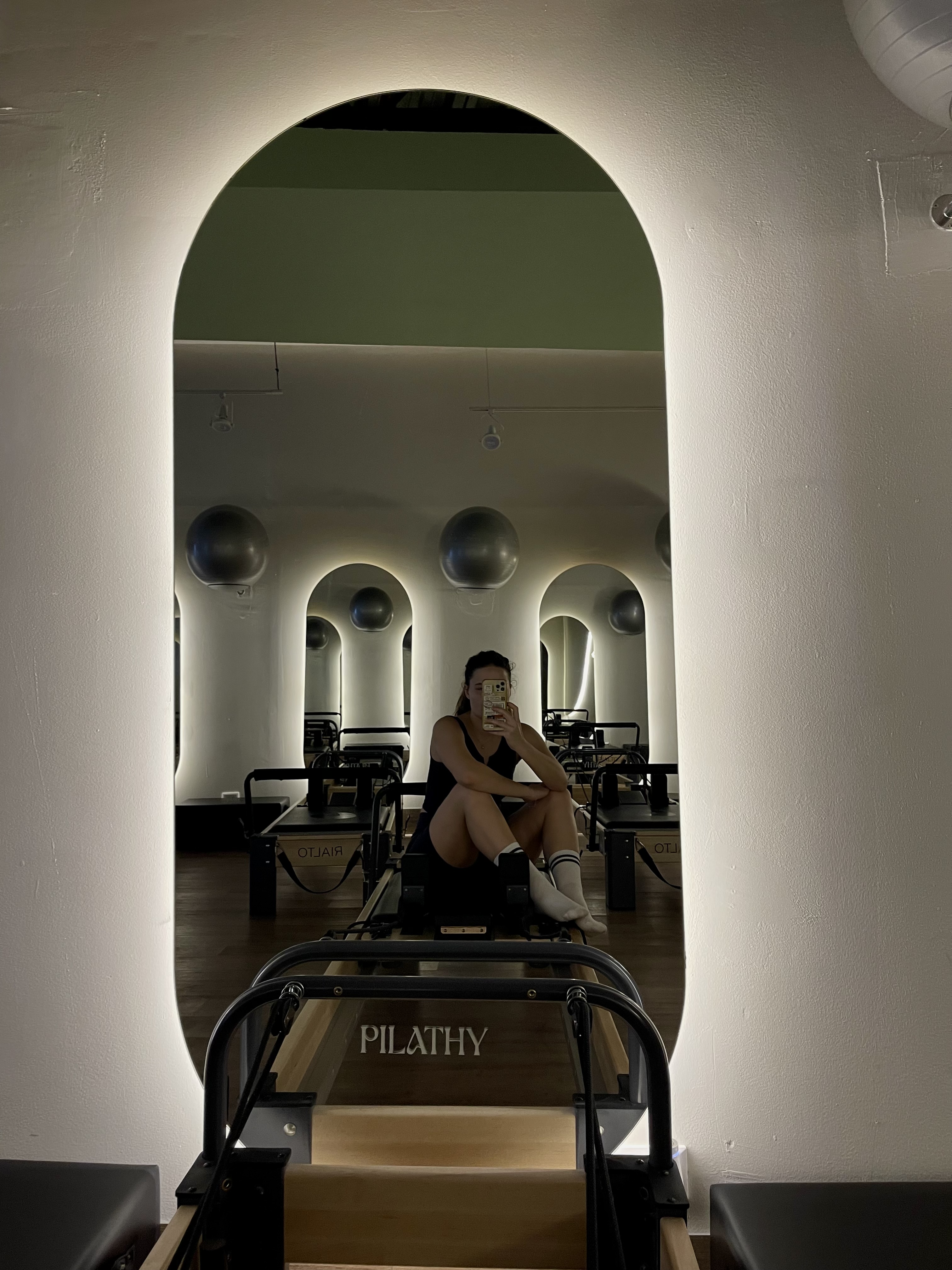 Person sitting on a Pilates reformer in a mirrored studio.