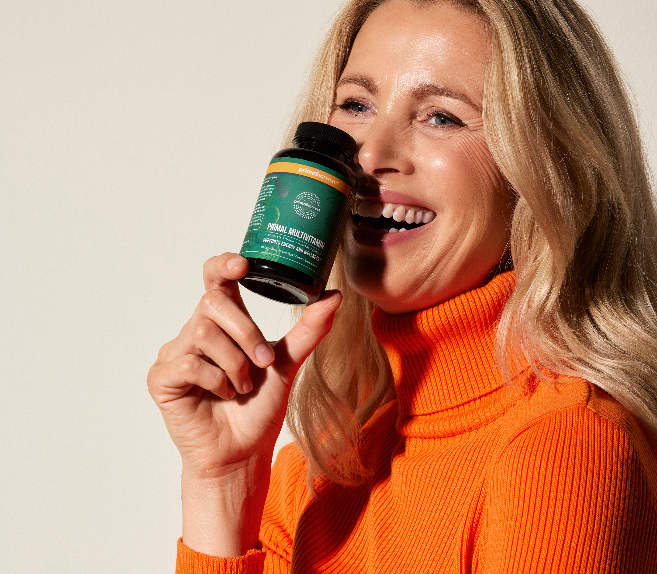 Smiling person in orange sweater holding a bottle of Primal Multivitamin.