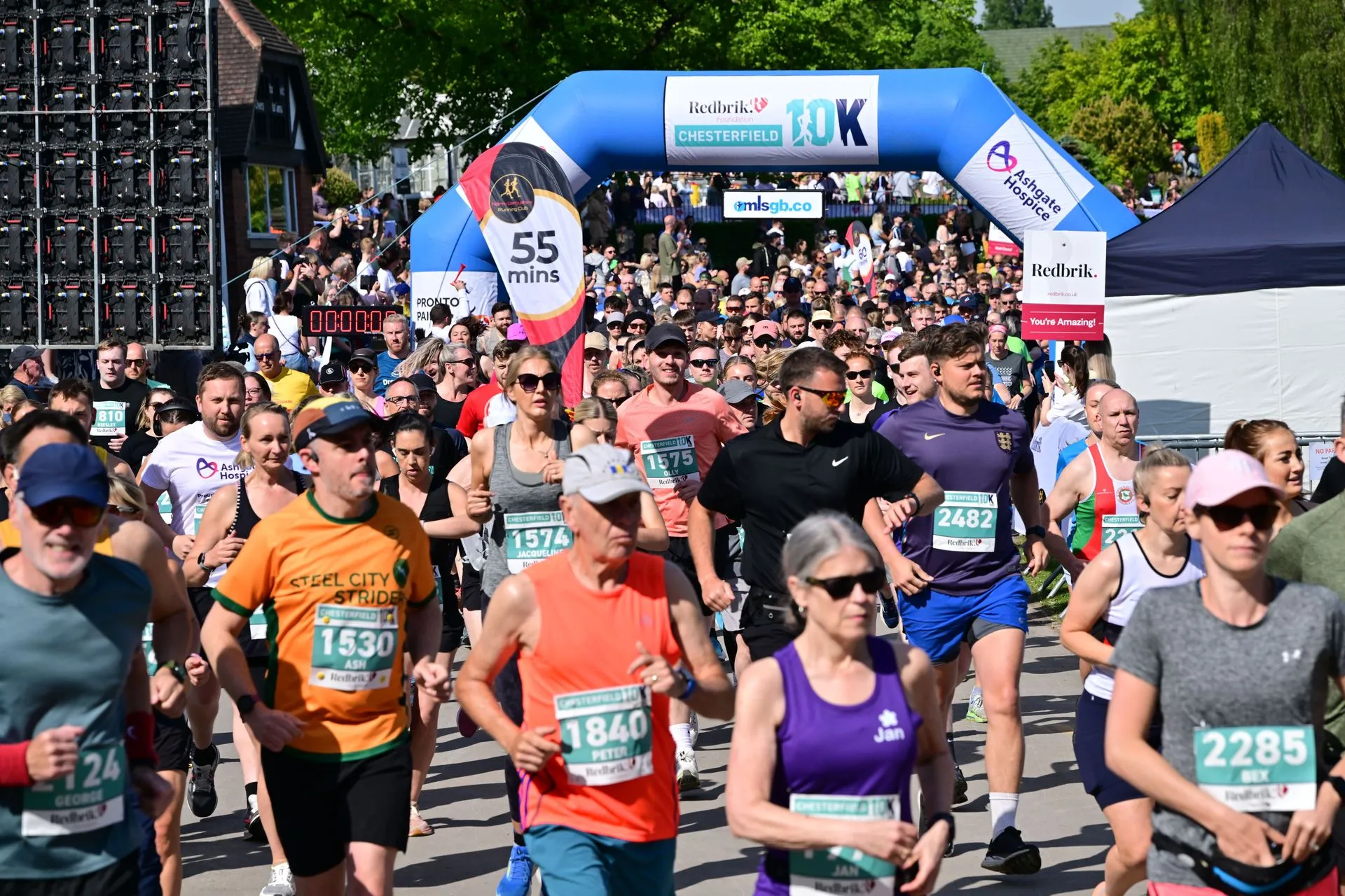 A large crowd of runners begins the Redbrik Chesterfield 10K race under a blue inflatable archway.