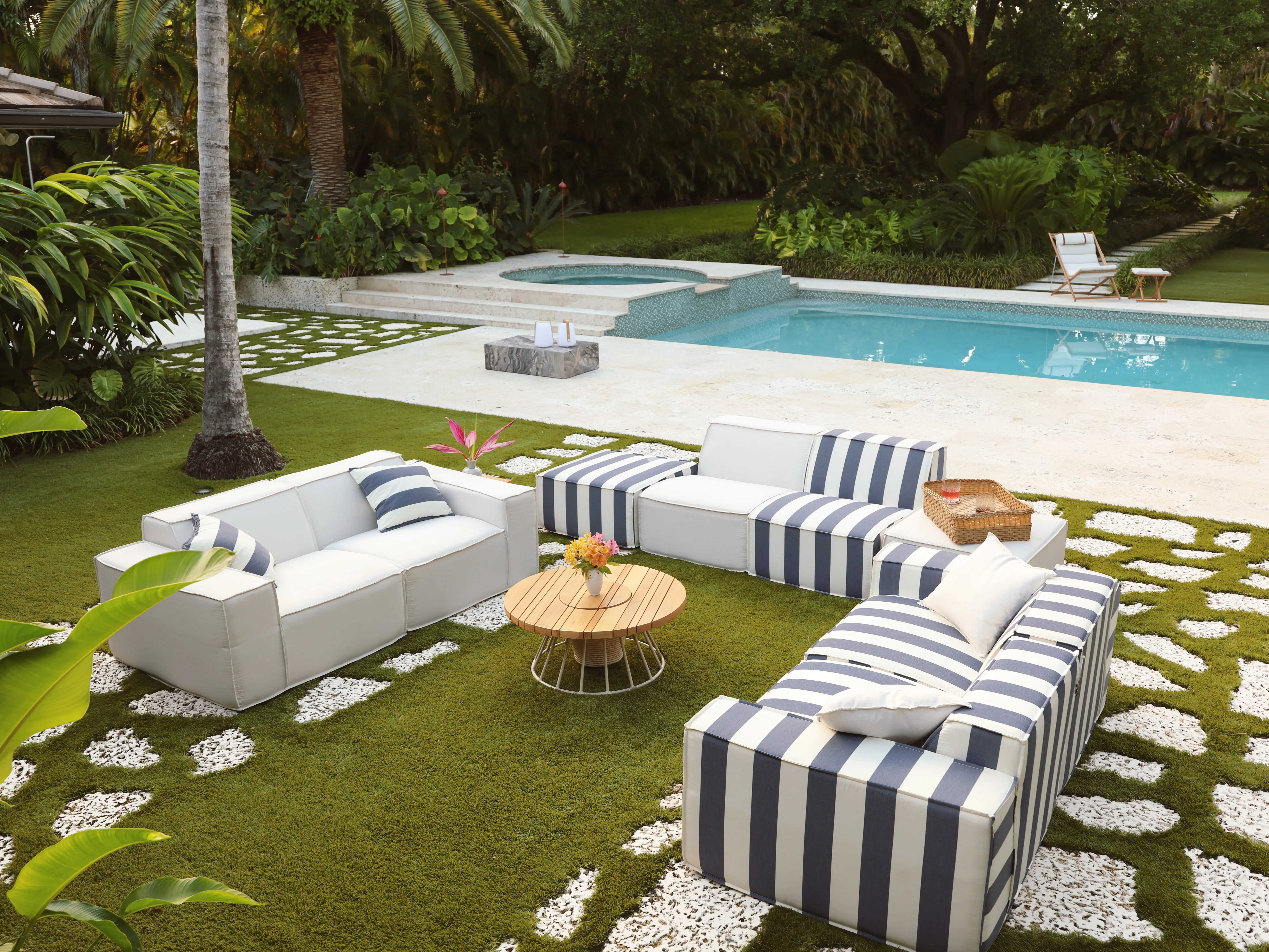 Modern white and striped outdoor sofas on a green lawn by a swimming pool and hot tub.