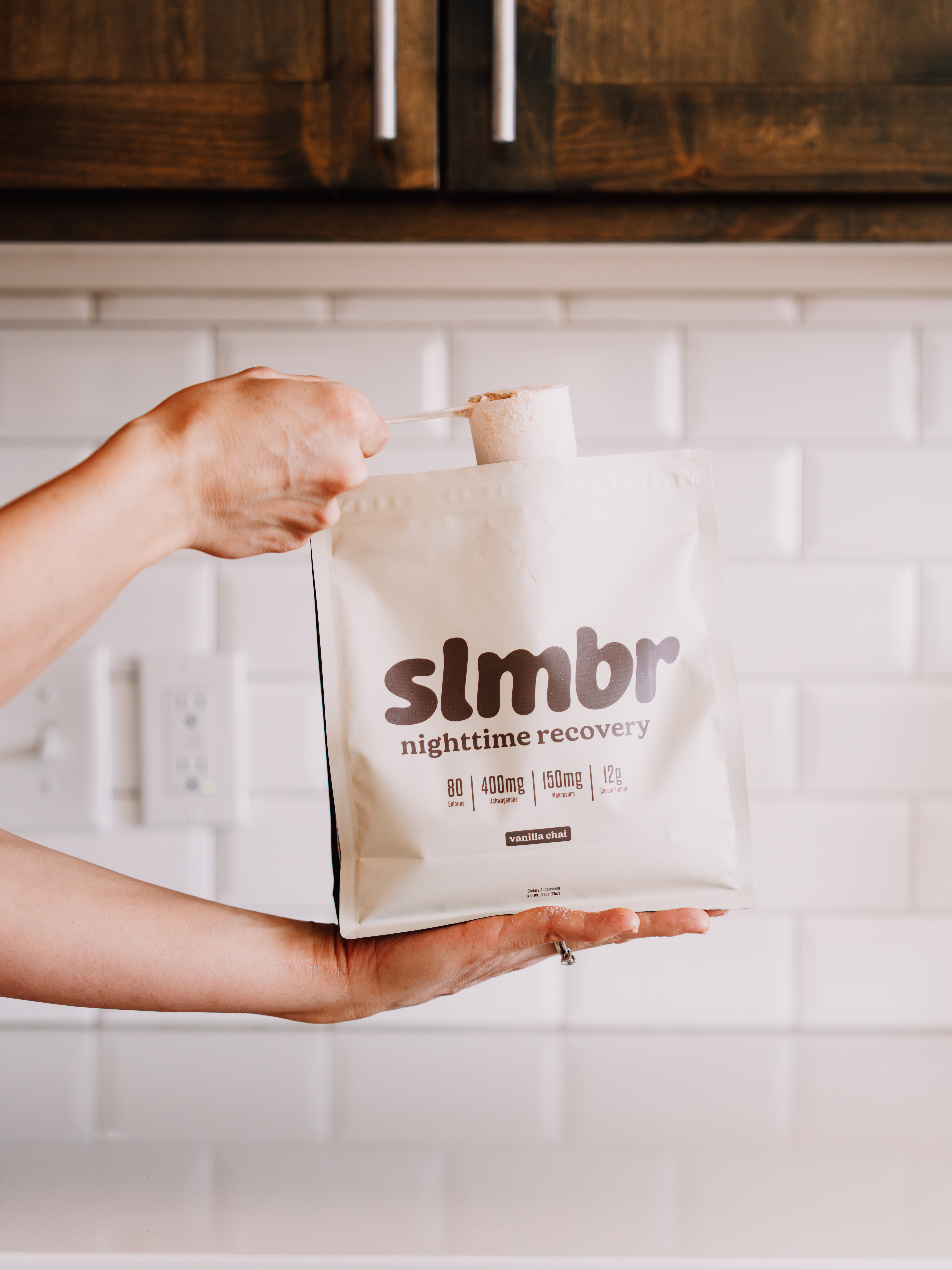 A person holds a white pouch of slmbr nighttime recovery powder and pulls out a scoop.
