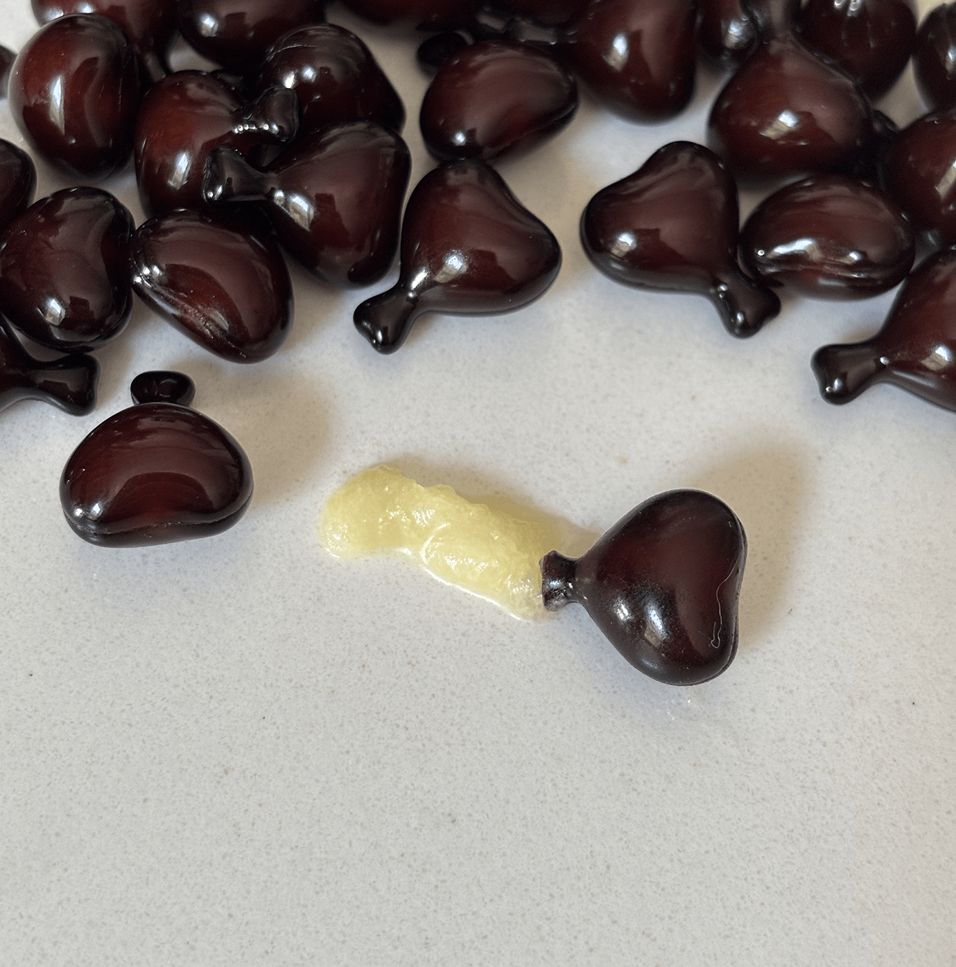 Dark heart-shaped capsules with one broken, releasing yellow substance.