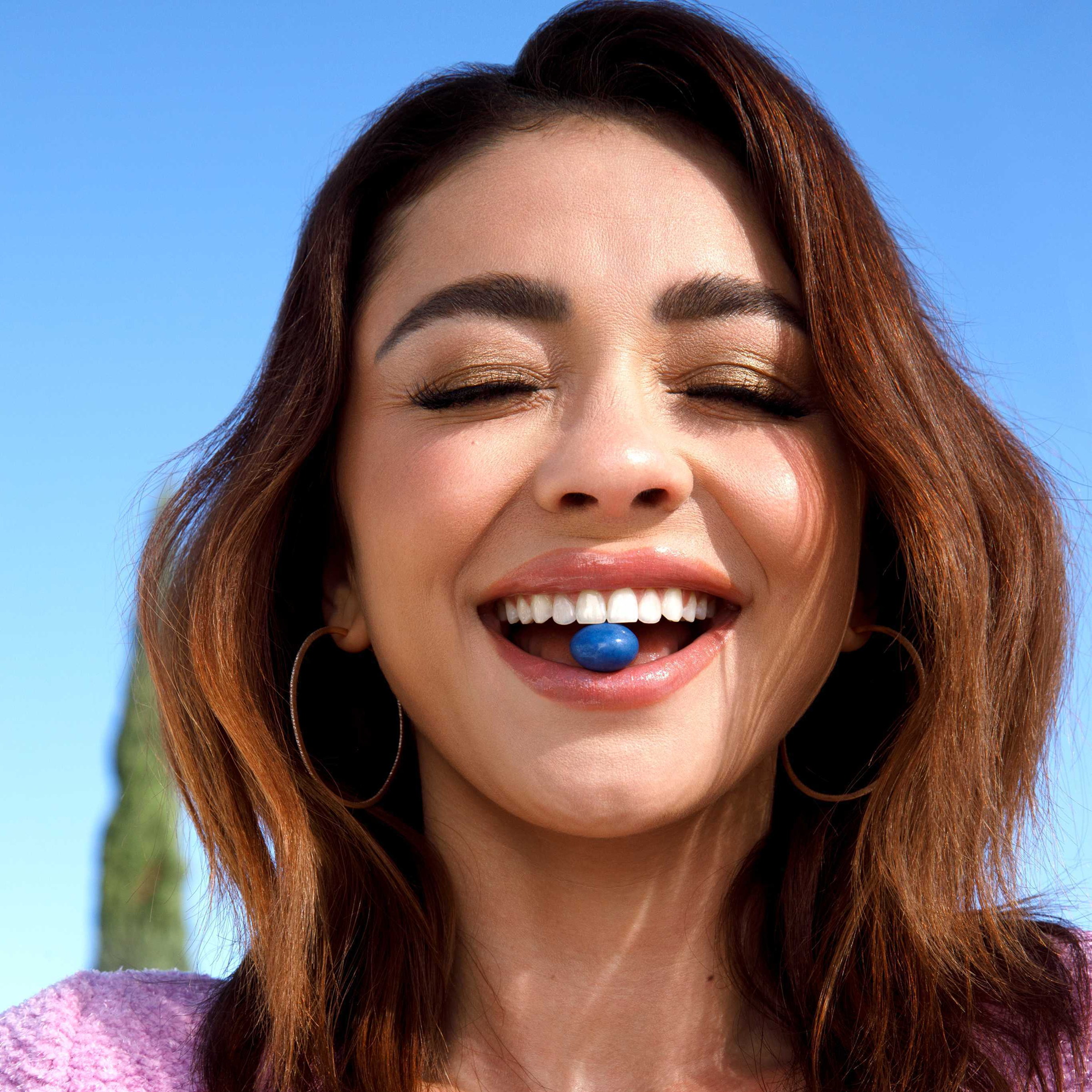 Person smiling with blue pill in their mouth, clear sky background.