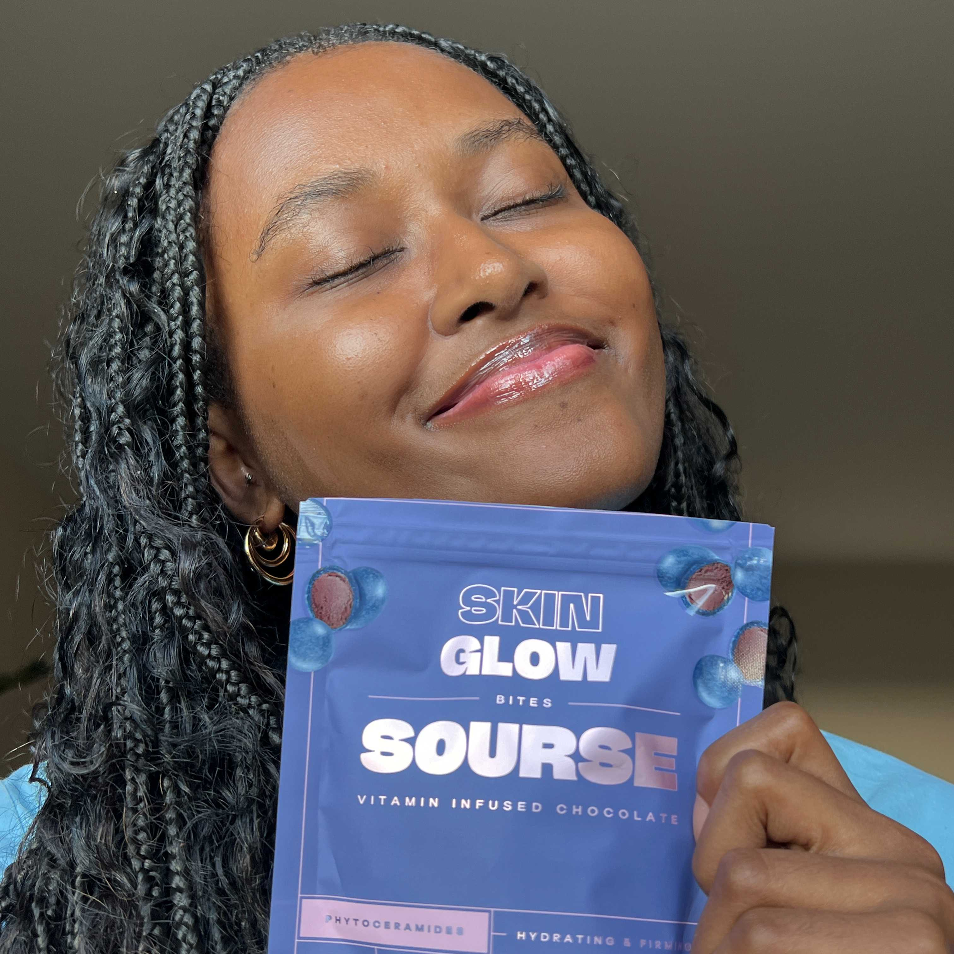 Person smiling, eyes closed, holding a packet of 'Skin Glow Bites Sourse' chocolate.