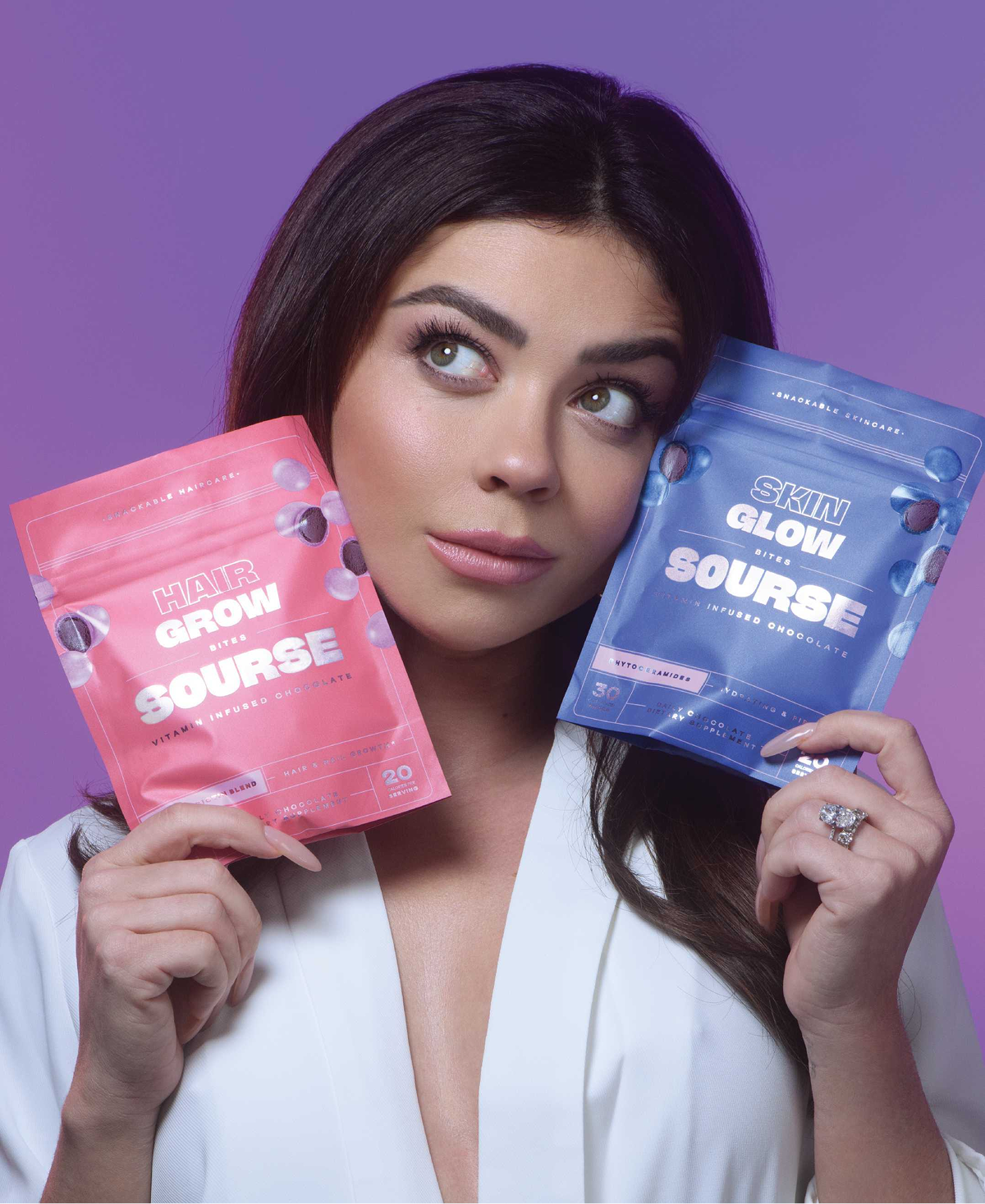 A woman holds two pouches of Sourse brand vitamin bites, one pink and one blue, against a purple background.