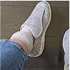 Person wearing gray slip-on shoes, knitted socks, and blue jeans on wooden floor.