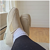 Feet in beige slip-on shoes resting on a light wooden floor.