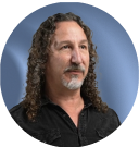 Man with long curly hair and beard, wearing a black shirt, against a blue background.