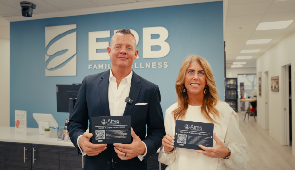 Three men stand together outdoors in a rural setting in front of a wooden fence.
