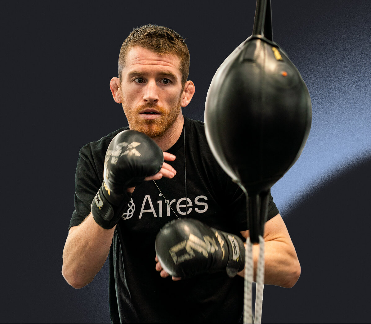 Man in black shirt with boxing gloves practices with punching bag.