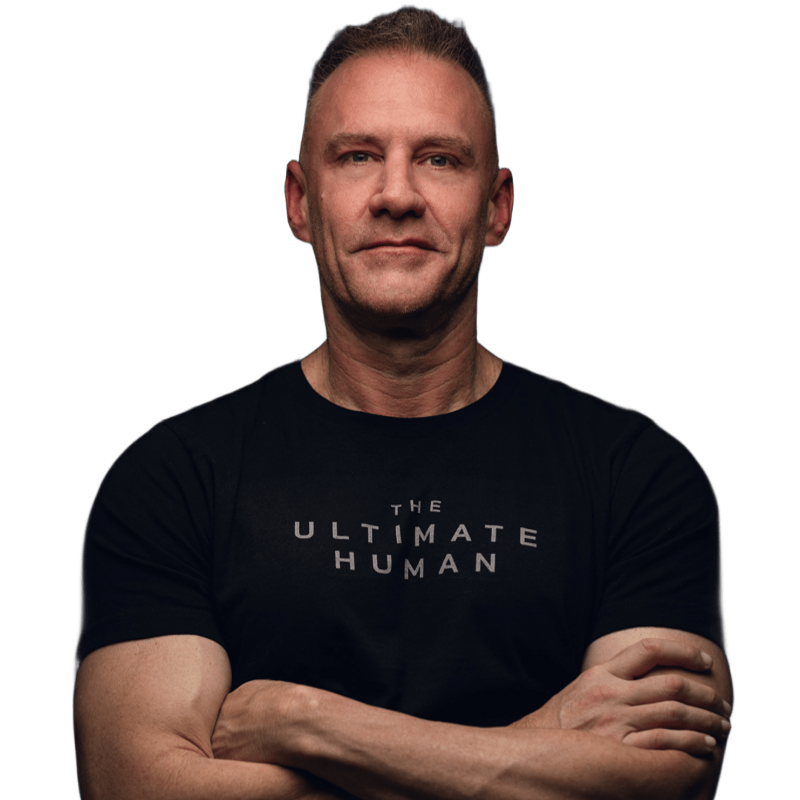 A man with short hair and crossed arms wearing a black t-shirt that reads, 'THE ULTIMATE HUMAN'.