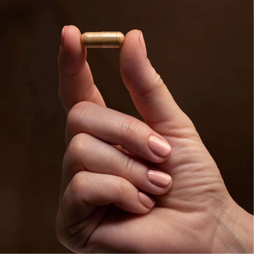A hand holding a small capsule between thumb and index finger.