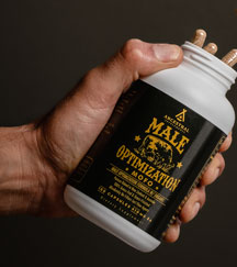 Hand holding a bottle labeled 'Male Optimization' with capsules inside.