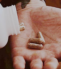 Hand holding capsules being poured from a bottle.