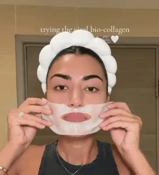 Person applying a sheet mask to their face, wearing a white headband.