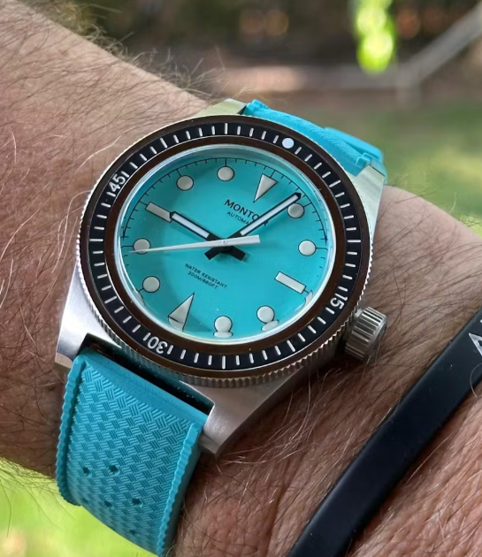 Turquoise wristwatch with a black bezel on a person's wrist.
